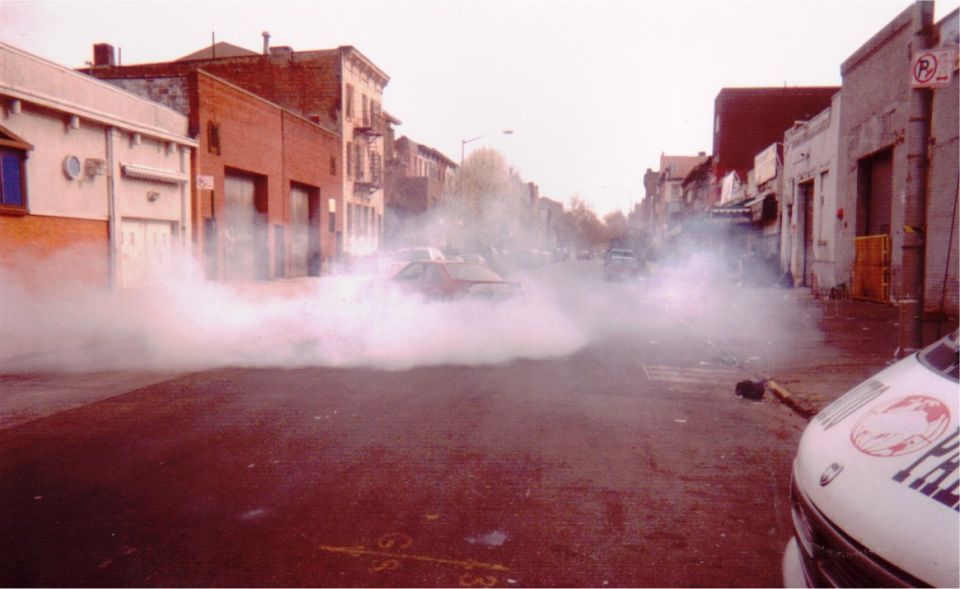 Red car doing a smoky burnout on a city street between brick buildings