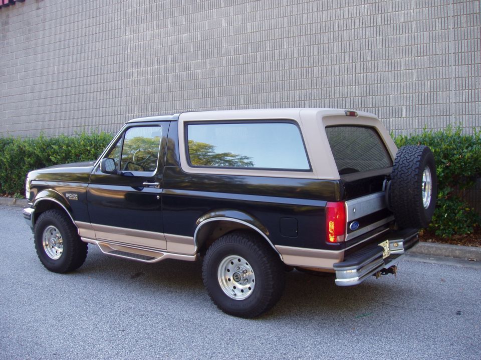 Black Ford Bronco with tan top and spare tire on back, parked on asphalt