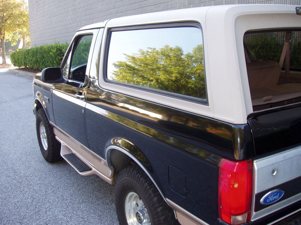 Black and tan Ford Bronco, rear three-quarter view, showing side steps and tinted windows