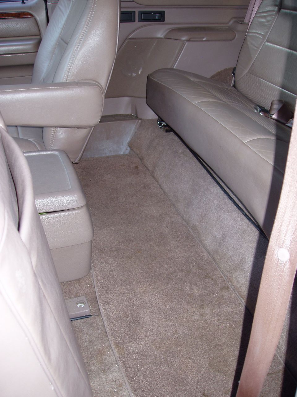 Interior view of a vehicle's back seat and floor, showing tan leather seats and carpet