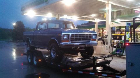 1979 Ford F-250 - A dark blue Ford pickup truck is being transported on a trailer at a gas station.