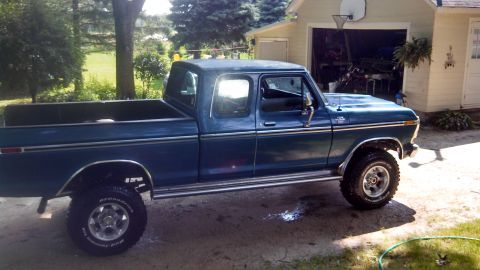 1979 Ford F-250 - A blue 1979 Ford F-250 pickup truck with lifted suspension and chrome trim is parked outside a garage.