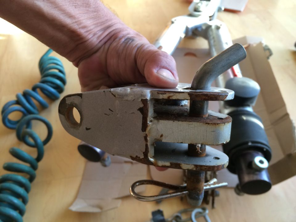 Rusty tow hitch part held by a hand, with a blue coiled cable and other parts in the background