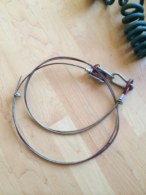 2003 Honda CR-V - A tow bar cable assembly with metal connectors lies on a wood-plank floor, next to a green coil spring.