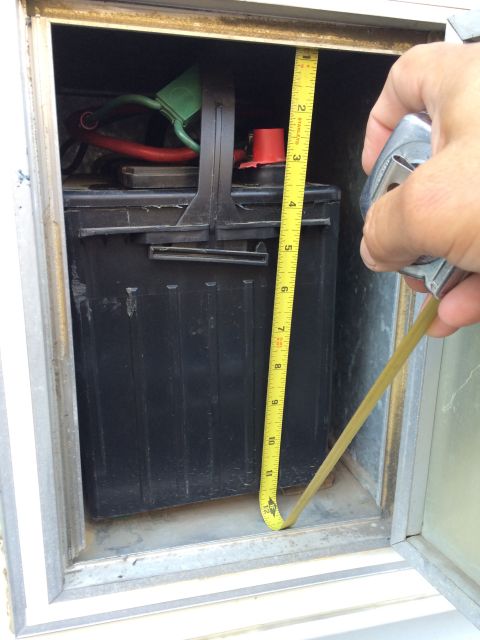 1986 Yugo GV - A tape measure is used to check the dimensions of a car battery housed within a compartment.