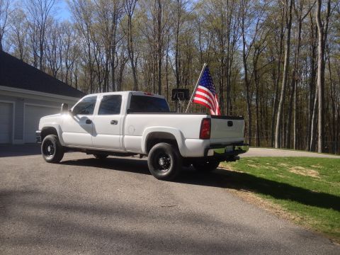 2006 Chevrolet Silverado 2500 - A white 2006 Chevrolet Silverado 2500 pickup truck is parked in a driveway with an American flag displayed in the truck bed.