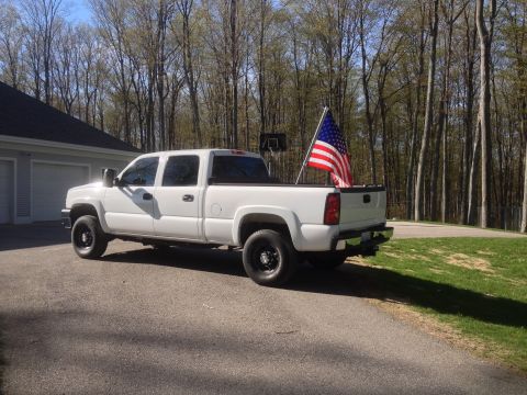 2006 Chevrolet Silverado 2500 - White Chevrolet Silverado pickup truck with an American flag in the bed, parked outside a house.