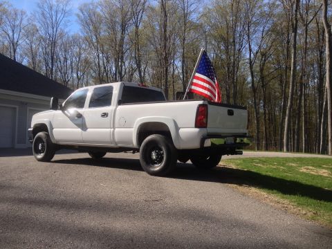 2006 Chevrolet Silverado 2500 - A white 2006 Chevrolet Silverado 2500 pickup truck is parked outside with an American flag in the bed.