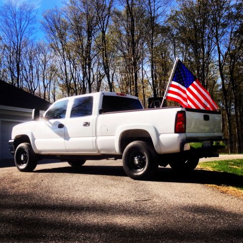 2006 Chevrolet Silverado 2500 - A white 2006 Chevrolet Silverado 2500 pickup truck is parked outside on a sunny day, with an American flag displayed in the truck bed.