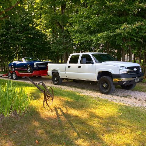 2006 Chevrolet Silverado 2500 - A white Chevrolet pickup truck tows a blue convertible on a trailer down a gravel driveway.