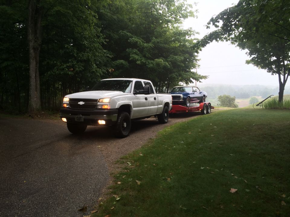 White 2006 Chevrolet Silverado 2500 towing a blue car on a trailer