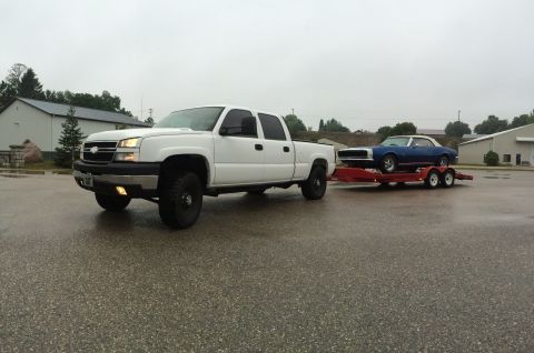 2006 Chevrolet Silverado 2500 - A white 2006 Chevrolet Silverado 2500 is seen towing a classic blue convertible on a trailer.