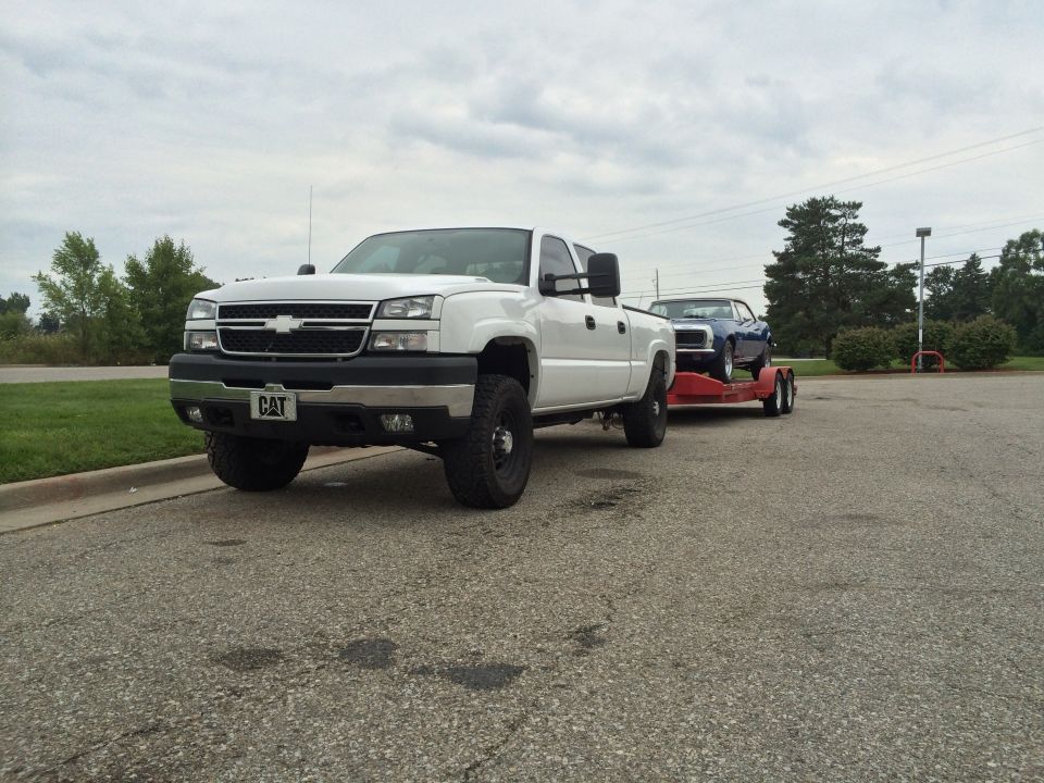 White 2006 Chevrolet Silverado 2500 towing a blue classic car on a red trailer