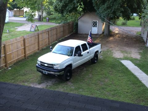 2006 Chevrolet Silverado 2500 - A white pickup truck is parked in a residential yard, with an American flag displayed in its bed.