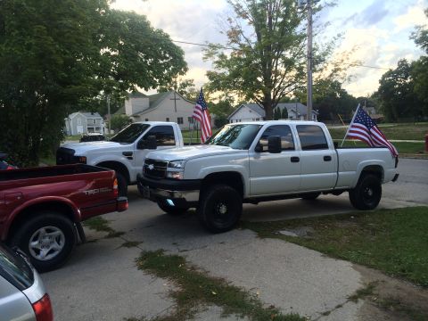 2006 Chevrolet Silverado 2500 - A white Chevrolet Silverado pickup truck is parked next to other vehicles, with an American flag displayed in its bed.
