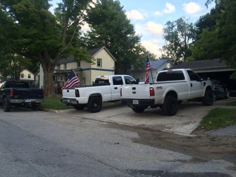 2006 Chevrolet Silverado 2500 - Three pickup trucks are parked on a residential street, two of which have American flags.