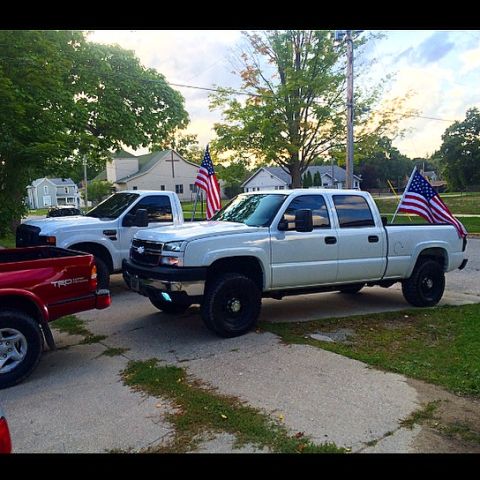 2006 Chevrolet Silverado 2500 - A white pickup truck flies American flags on either side of its bed.
