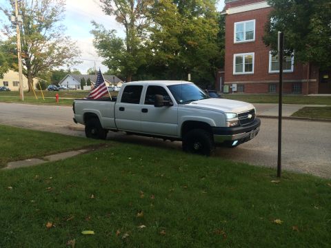 2006 Chevrolet Silverado 2500 - A white 2006 Chevrolet Silverado 2500 pickup truck is parked on a residential street, displaying American flags in its bed.