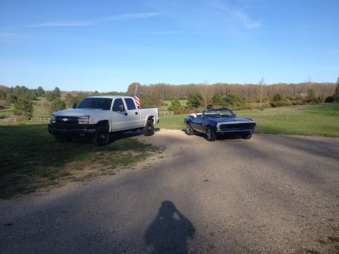 2006 Chevrolet Silverado 2500 - A white pickup truck and a blue convertible are parked on a gravel driveway with trees in the background.