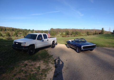 2006 Chevrolet Silverado 2500 - A white 2006 Chevrolet Silverado 2500 is parked on a dirt road next to a classic blue convertible under a clear sky.