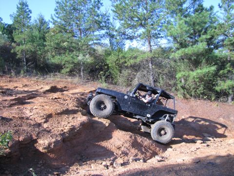 1995 Ford Bronco - This modified off-road vehicle navigates a challenging incline on a dirt trail surrounded by trees.