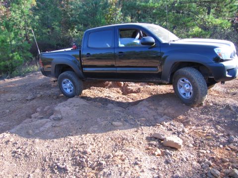 1995 Ford Bronco - A black Toyota Tacoma navigates a challenging off-road trail, with its tires on uneven ground.