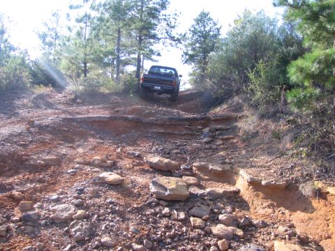 1995 Ford Bronco - A black pickup truck navigates a challenging, rocky terrain on an off-road trail.