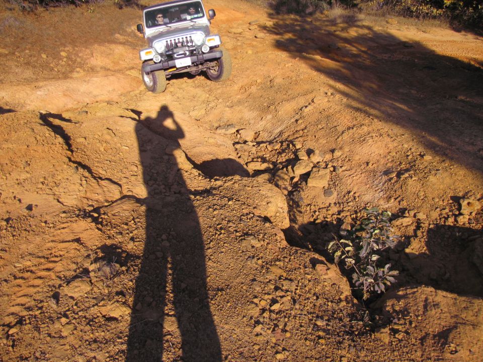 Jeep Wrangler driving on a rocky, dirt trail. A person is taking the photo