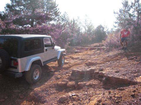 1995 Ford Bronco - A silver Jeep Wrangler navigates a challenging off-road path with a person walking in the background.