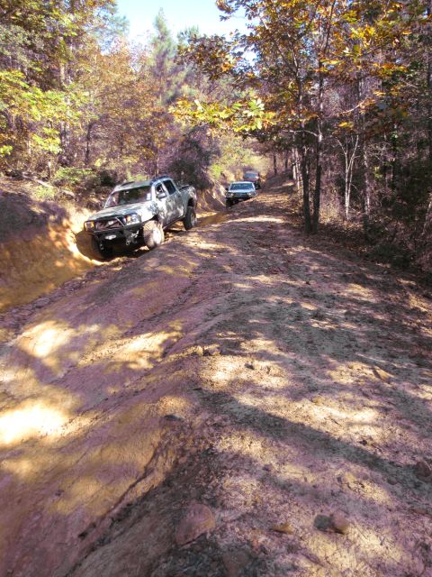 1995 Ford Bronco - Multiple off-road vehicles navigate a challenging dirt path in a forest setting.