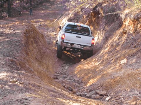 1995 Ford Bronco - Pickup truck tackling a challenging off-road path with steep, eroded sides.