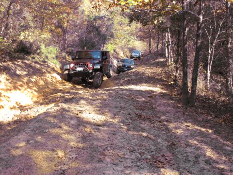 1995 Ford Bronco - Multiple vehicles navigate a challenging dirt path surrounded by trees and autumn foliage.