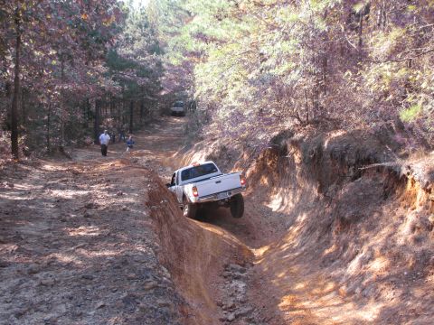 1995 Ford Bronco - A white pickup truck tackles a challenging off-road course with another vehicle visible in the distance.