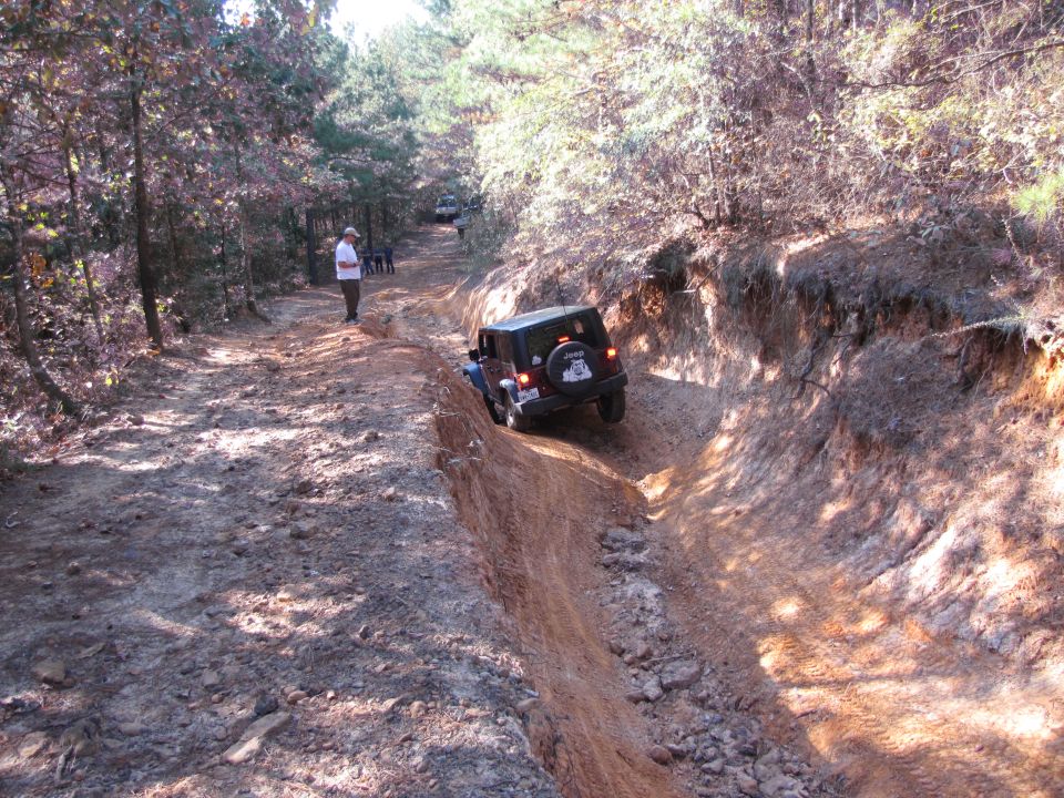 Dark colored Jeep Wrangler on a dirt trail, rear view. Spare tire visible on back