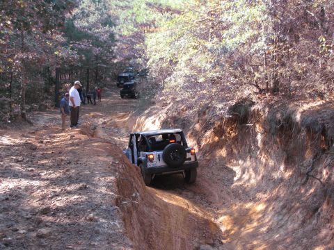 1995 Ford Bronco - Multiple off-road vehicles navigate a challenging dirt path through a wooded area.