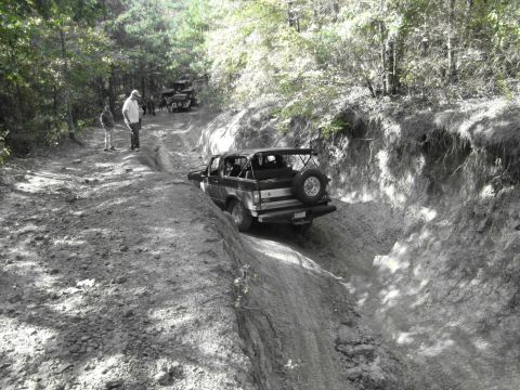 1995 Ford Bronco - A black 1995 Ford Bronco navigates a challenging off-road trail with other vehicles visible in the background.