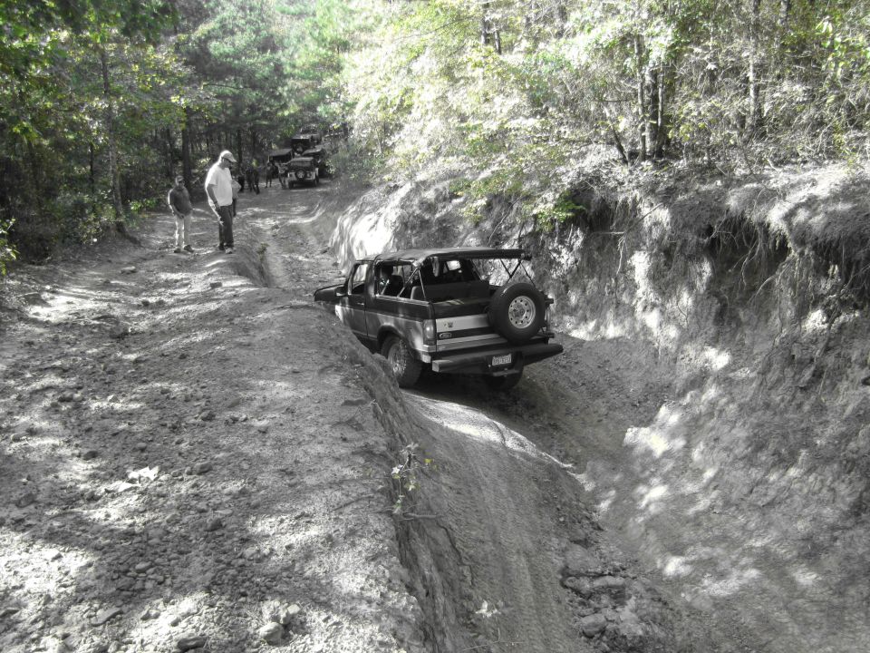Black 1995 Ford Bronco driving off-road on a dirt trail, spare tire mounted on rear