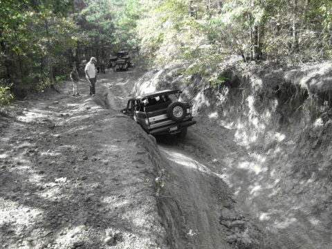 1995 Ford Bronco - Several vehicles tackle a challenging off-road trail, with one Bronco navigating a deep rut.