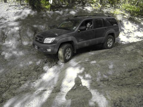 1995 Ford Bronco - A dark SUV navigates a challenging dirt trail, with a driver visible behind the wheel.