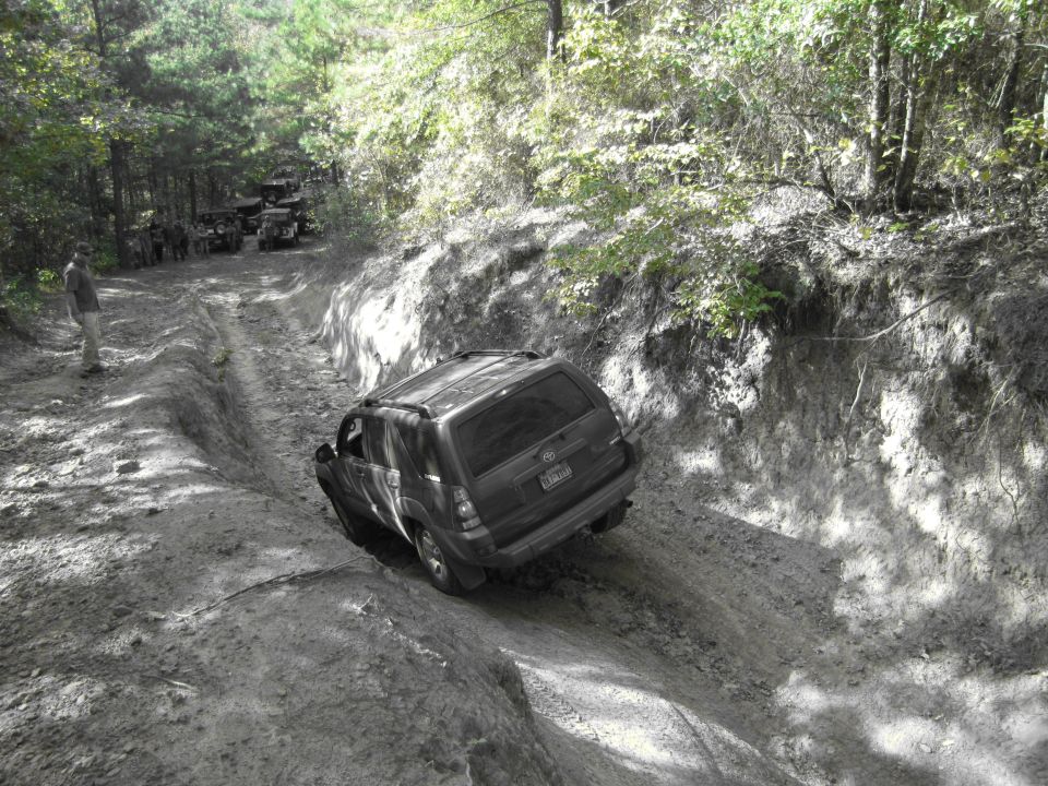 Dark SUV navigating a rutted dirt trail with other vehicles in the background