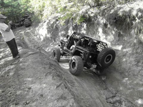 1995 Ford Bronco - A group of off-road vehicles navigate a challenging dirt path on a wooded hillside.