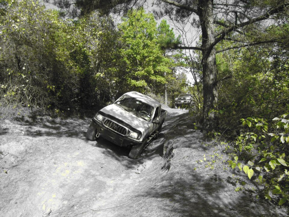 Silver pickup truck with aftermarket bumper and off-road tires navigating a dirt trail