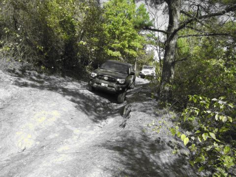 1995 Ford Bronco - Two off-road vehicles navigate a challenging trail through a wooded area.