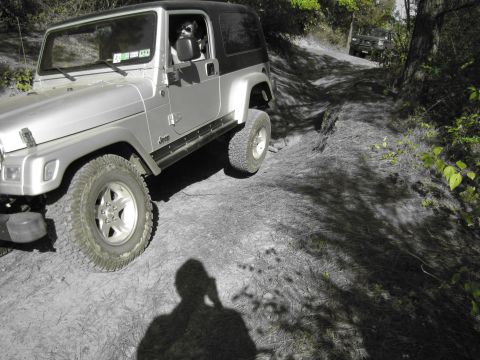 1995 Ford Bronco - A silver Jeep Wrangler navigates a dirt path with another vehicle following behind.