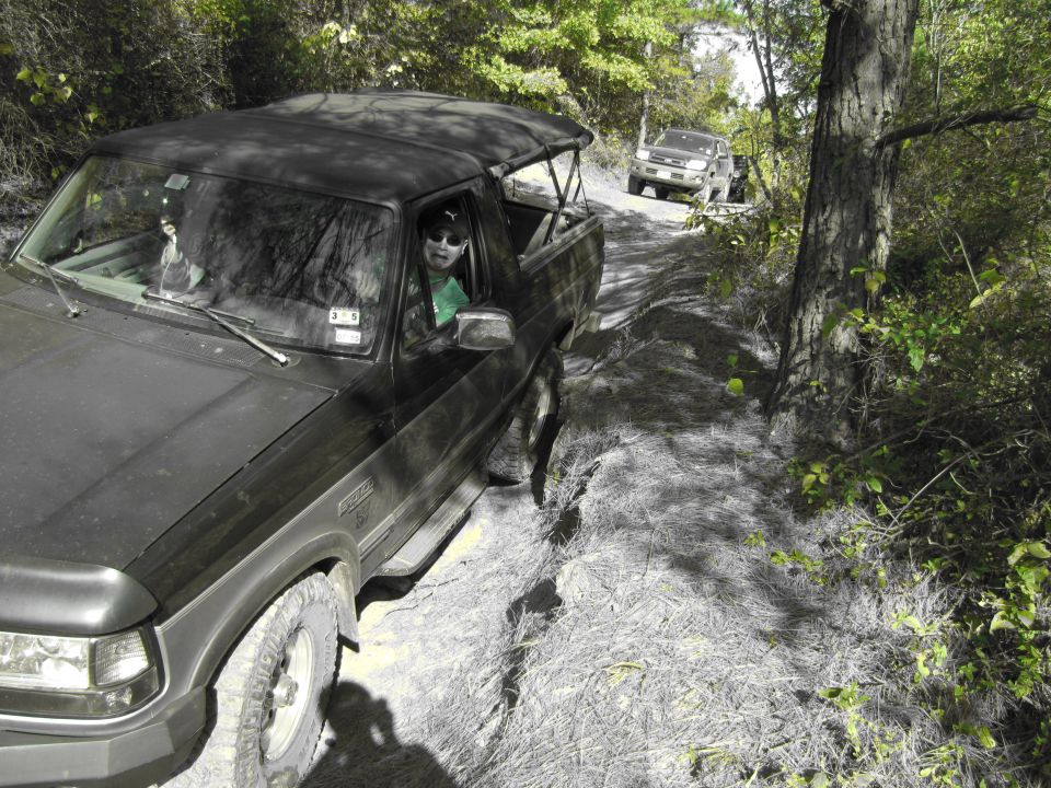 Black 1995 Ford Bronco driving on a dirt trail with another SUV behind it