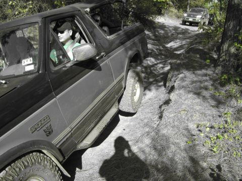 1995 Ford Bronco - Two SUVs, including a 1995 Ford Bronco, navigate a wooded trail during an off-road excursion.