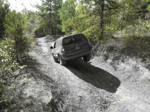 1995 Ford Bronco - A dark SUV navigates a steep dirt path, its rear end angled towards the camera. The vehicle appears to be from around 2003.