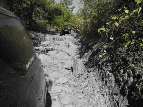 1995 Ford Bronco - A black SUV navigates a challenging rocky trail, with another off-road vehicle visible ahead.
