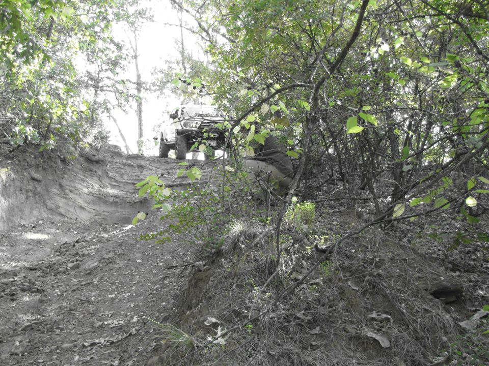 Off-road vehicle climbing a steep, muddy trail through trees