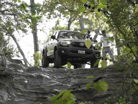 1995 Ford Bronco - A black pickup truck tackles a challenging muddy incline, with a person observing the off-road action.